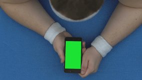 Sportsman watching online fitness video, lying smartphone on mat, workout break