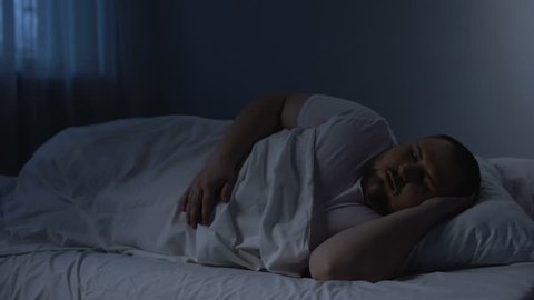 Fat sleeping man tossing in bed, health problem caused by excess weight, apnoe