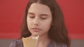 Pretty baby girl kid eating slow motion video nursing bottle licking big ice lifestyle cream in waffle cone with raspberry happy laughing on red background. the girl teenager and ice cream concept