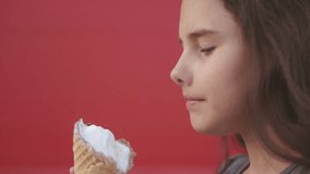 Pretty baby girl kid eating slow motion video nursing bottle licking big ice cream in waffle cone with raspberry lifestyle happy laughing on red background. the girl teenager and ice cream concept