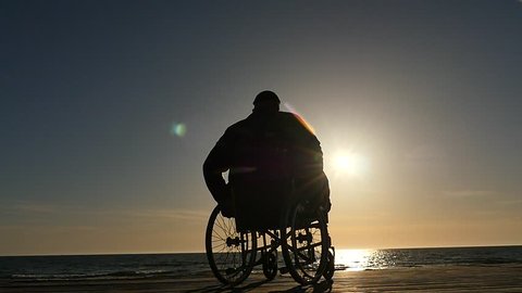 man in wheelchair silhouette near sea horizon at sunset