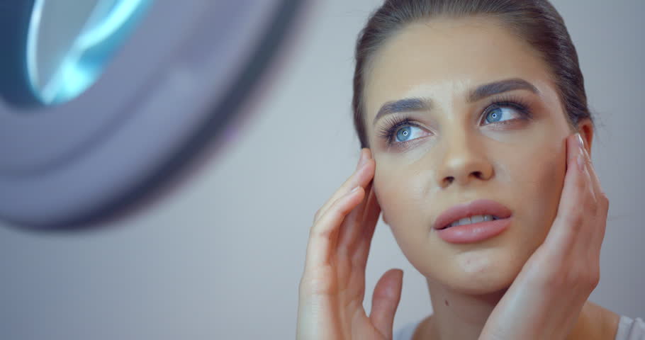 Pretty young blue eyed girl with porcelain fresh skin and natural make-up is admiring her look in mirror. 4k footage. She is touching her face. | Shutterstock HD Video #1011233819