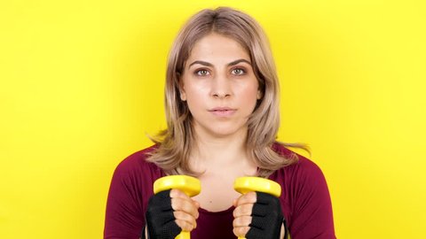 Woman on yellow background practicing sport with dumbbells. Fit and healthy girl
