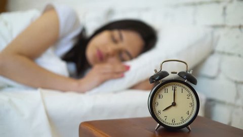 Tired brunette turning off her alarm clock in her bedroom.