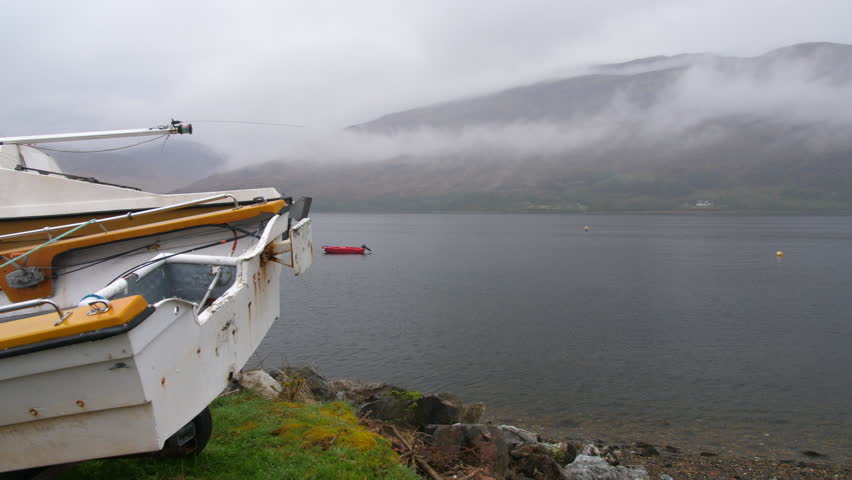 4K Red boat and moored boat on a lake in the Scottish Highlands Fort Williams Loch Linnhe. Calm water with fishing vessel and buoyed within a natural gentle river in rural noir Scotland.
