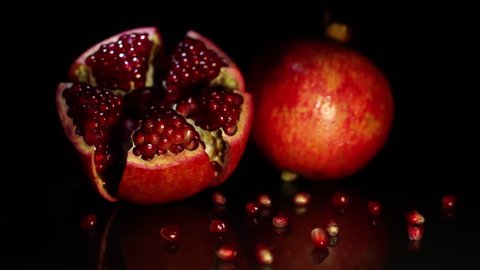 Two fruit pomegranates lie on a black table on a black background. HD