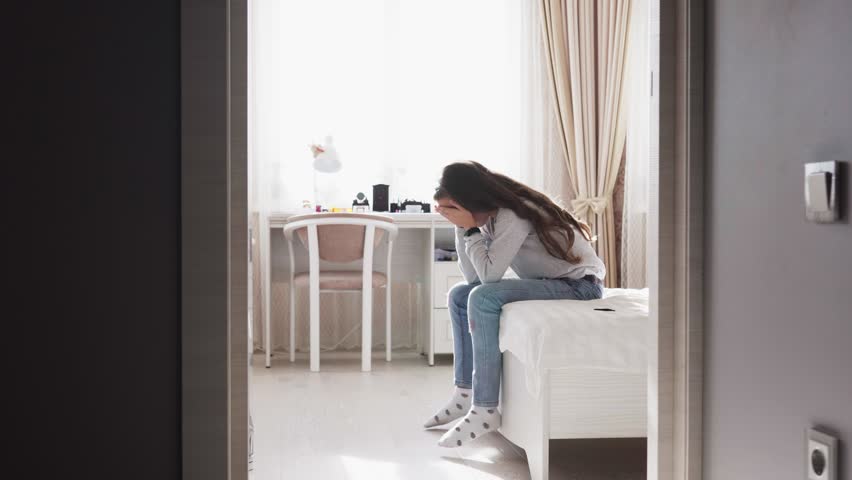 Sad child sitting on bed close her face with hands, zoom in