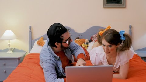 An odd couple (actors in character as kids): a guy and a girl on the bed, watching porn movies on a laptop, feeling the urge to vomit as it's not what they expected. Funny bizarre medium shot.
