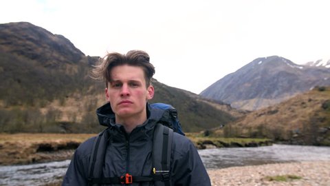 4K Portrait of handsome traveller standing in front of Ben Nevis mountain in Scottish Highland. Hiker and backpacker in front of river in front of Scotland UK 
