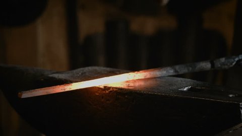 Blacksmith manually forging the molten metal on the anvil in smithy with spark