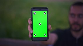 Young Man Holding Smartphone with empty green screen, outdoors 