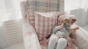 Little girl and dog playing together. Slow motion. Beautiful baby play wit her dog in the armchair