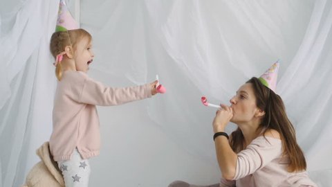 Slow motion shot of little cutey girl and her beautiful mother wearing festive cap and blows horn