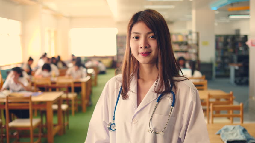 Advertising, Education, Business, Healthcare and Medical Concept - Portrait of Beautiful young asian medical doctor with attractive smile and stethoscope looking at camera in library.