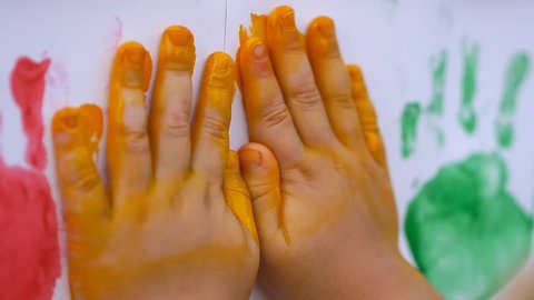 Close up of little child's hands making color handprints in the white wall in slow motion 50fps