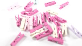 4k wooden coloured clothes pegs on a white surface background. moving close up image of pink purple and cream pastel craft and handicraft supplies for school office or play.