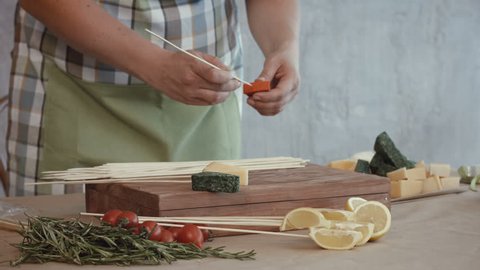 Midsection of cooking woman pinning slices of assorted types of cheese and cherry tomatoes on wooden skewers in the kitchen while creating edible bouquet arrangement for a gift.