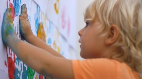 Close up of happy little child making colorful handsprint on the white wall with mother together. Slow motion 50fps