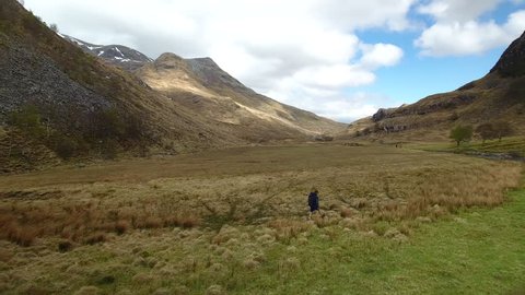 4K Man walking through the Scottish Highlands. A mountain hiker in a summer tourist landscape with blue sky and clouds over a rural Scotland countryside 