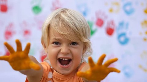 A little cute happy child scaring by hands in colorful print and smiling on color handprints background in slow motion 50fps