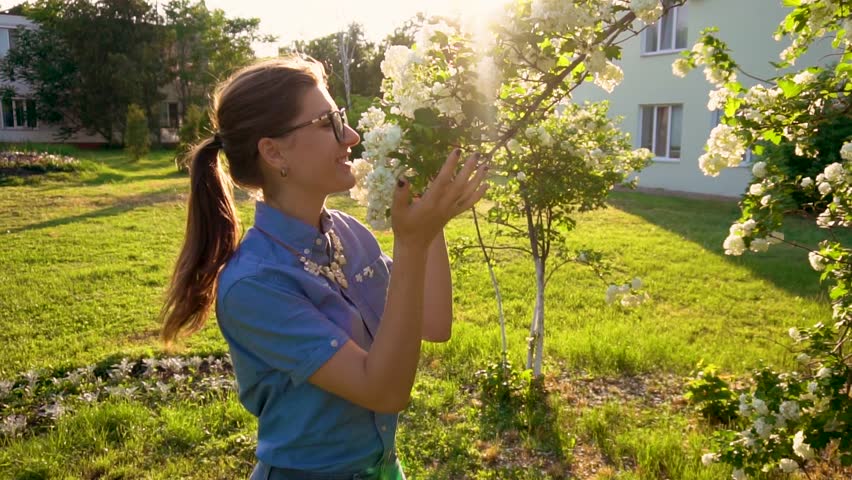 Happy young beautiful women sniff the bloom in slow motion in summer park.