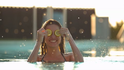 Young woman holding fruits slices on eyes while being splashed