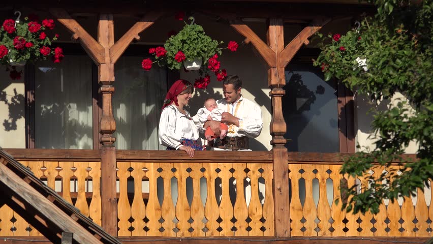 Man, woman and baby with traditional clothes at wooden house balcony, parents kissing child, family portrait