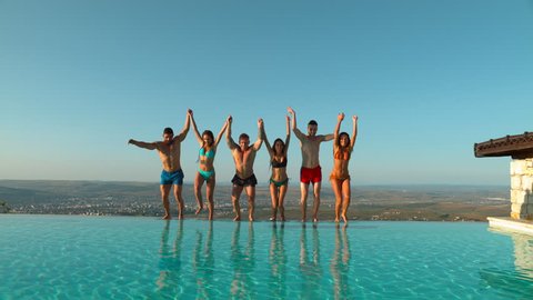 Friends holding hands and jumping in water at a pool party