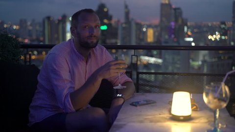 Portrait of happy man drinking cocktail sitting in skybar at night
