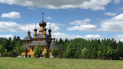 Horses walking on the field near Church Of The Holy Prophet John The Baptist in Dudutki Museum Complex in Belarus. Panoramic view
