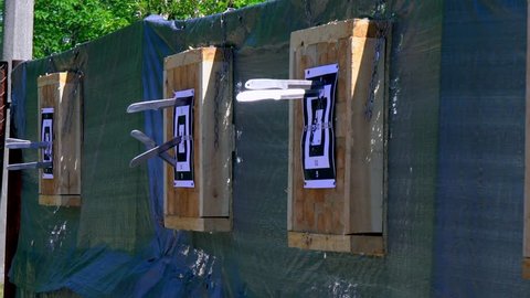 Throwing knives at the target from an open-air distance, a competition for throwing knives, flying knives, sharp knives fly in a target from the wood stands, slow motion