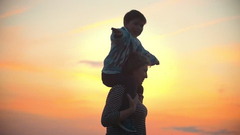 Woman and her children. Child show the plane with their hands. Mother and her little son have fun against the scarlet sunset Mother holds child on shoulders they're spinning.