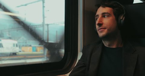 Man riding train listening to music, podcast, or audiobook while riding train  and looking out window