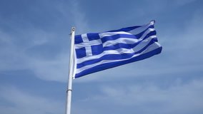 Slow motion video of Greek flag waving on slightly cloudy blue sky as seen in Greek island of the Aegean