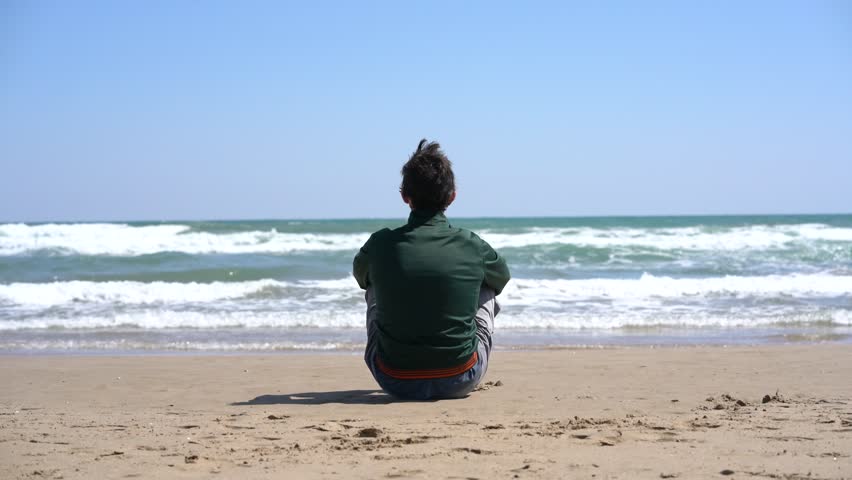 Man sitting on beach sand contemplates the sea.