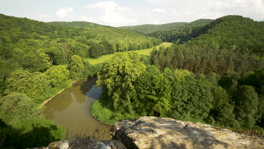 Panning shot across deep river valley landscape with lush green forest and meadows on river banks. View from mountain top on river horseshoe bend. 4k Ultra hd resolution.