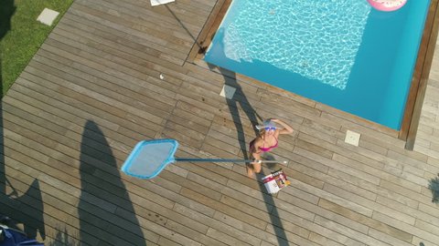 SLOW MOTION, POV, AERIAL: Blonde woman chasing around drone invading her privacy while she sunbathes in her garden. Funny angry girl next door throwing things at remote controlled plane stalking her.