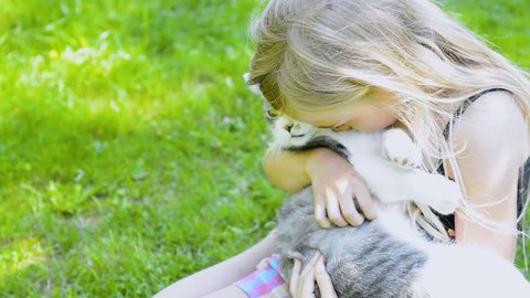 Cute little child blond girl with cat, girl playing with cat on the green grass lawn in the summer garden 
