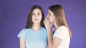 Young thin girl in white t-shirt telling a rumour to pretty brunette in light blue t-shirt, isolated shot in the purple background, concept of great amazement after received information