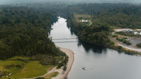 Drone shot of bridge over wide river surrounded by dark green trees beside the New Zealand coast.