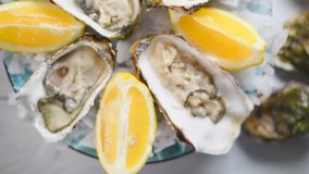 Fresh Oysters close-up rotating in blue plate, served table with oysters, lemon and ice. 4K Ultra high definition 3840X2160. Rotation 360 degrees