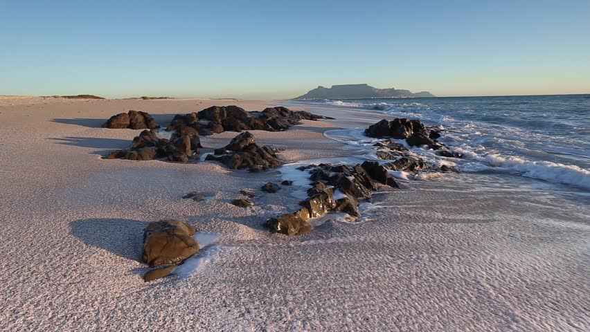 Wide angle view of waves washing up on the sandy beach and crashing against the rocks at Blouberg beach with a view of table mountain in cape town south africa