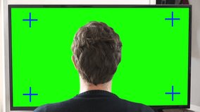 Zoom In Man Watching TV Television Green Screen. Young man watching big green screen television at home, zoom out. Shot behind model shoulders.