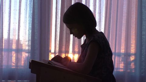 Young cute girl silhouette reading book in classroom at the sunset