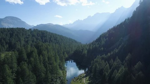 moving forward to pine woods forest lake and mountain valley with sun flare in summer day.Europe Italy Alps outdoor green nature scape mountains wild aerial establisher.4k drone establishing shot