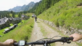 POV man riding e-bike to town village.Mtb action cyclist exploring path near mountains.Electrical bike active people sport travel vacation in Europe Italy Alps outdoors in summer.4k video