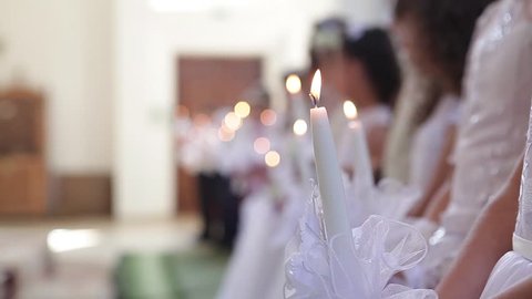 Children take the first communion in the church in white dresses holding candles in their hands.
