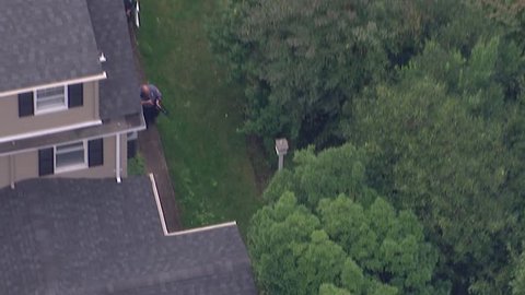 Aerial video of tactical police officer SWAT team on man hunt searching for criminal through house backyard neighborhood during day time