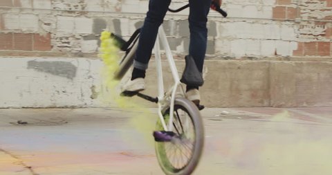 Close up of extreme BMX biker doing 360 spin  with purple and yellow colored smoke grenade trick in urban environment