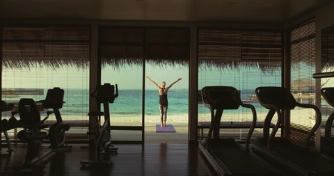 Back View Shot of a Fit Young Woman Doing Yoga on a Porch of a Gym Hut. In the Background Exotic Island with Beautiful Calm Sea and Clear Sunny Sky. Shot on RED Epic 4K UHD Camera.